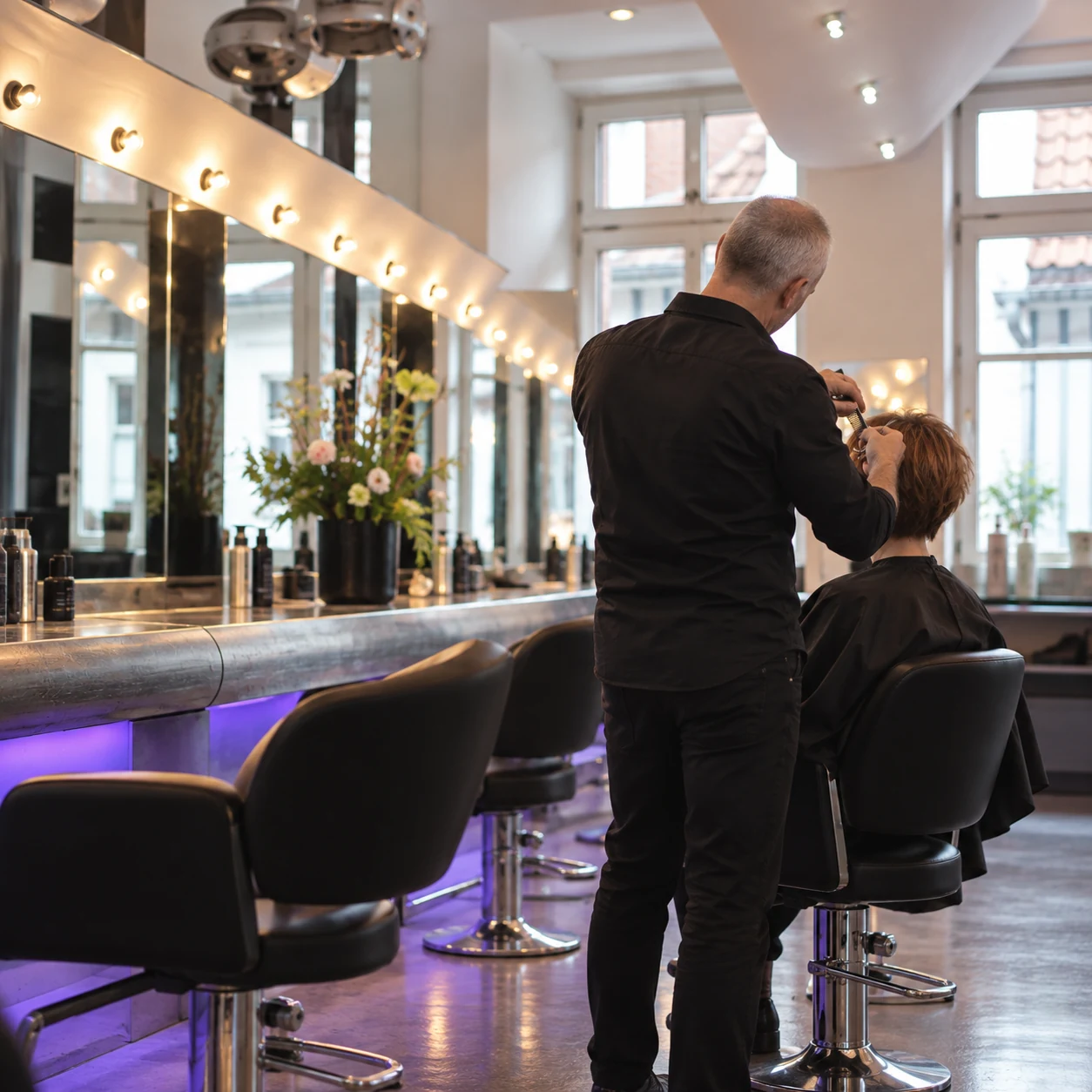 KI-Fotoidee: Blick in den Salon mit Boris von hinten beim Haareschneiden an einer Kundin